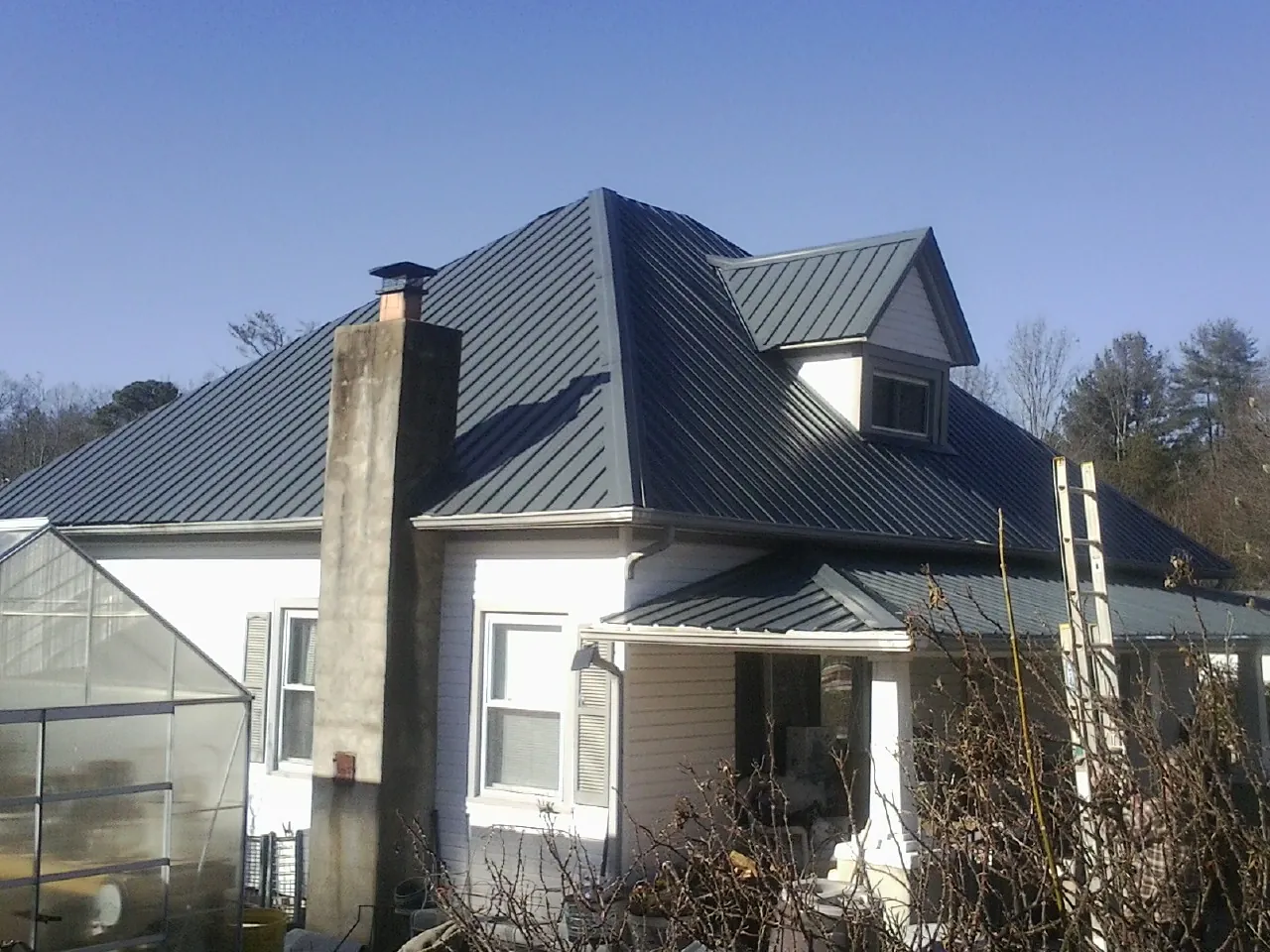 Dark blue standing seam metal roof on a white farmhouse with dormer — Slate & Tile Roof Repair by Roofing Brothers in House Springs