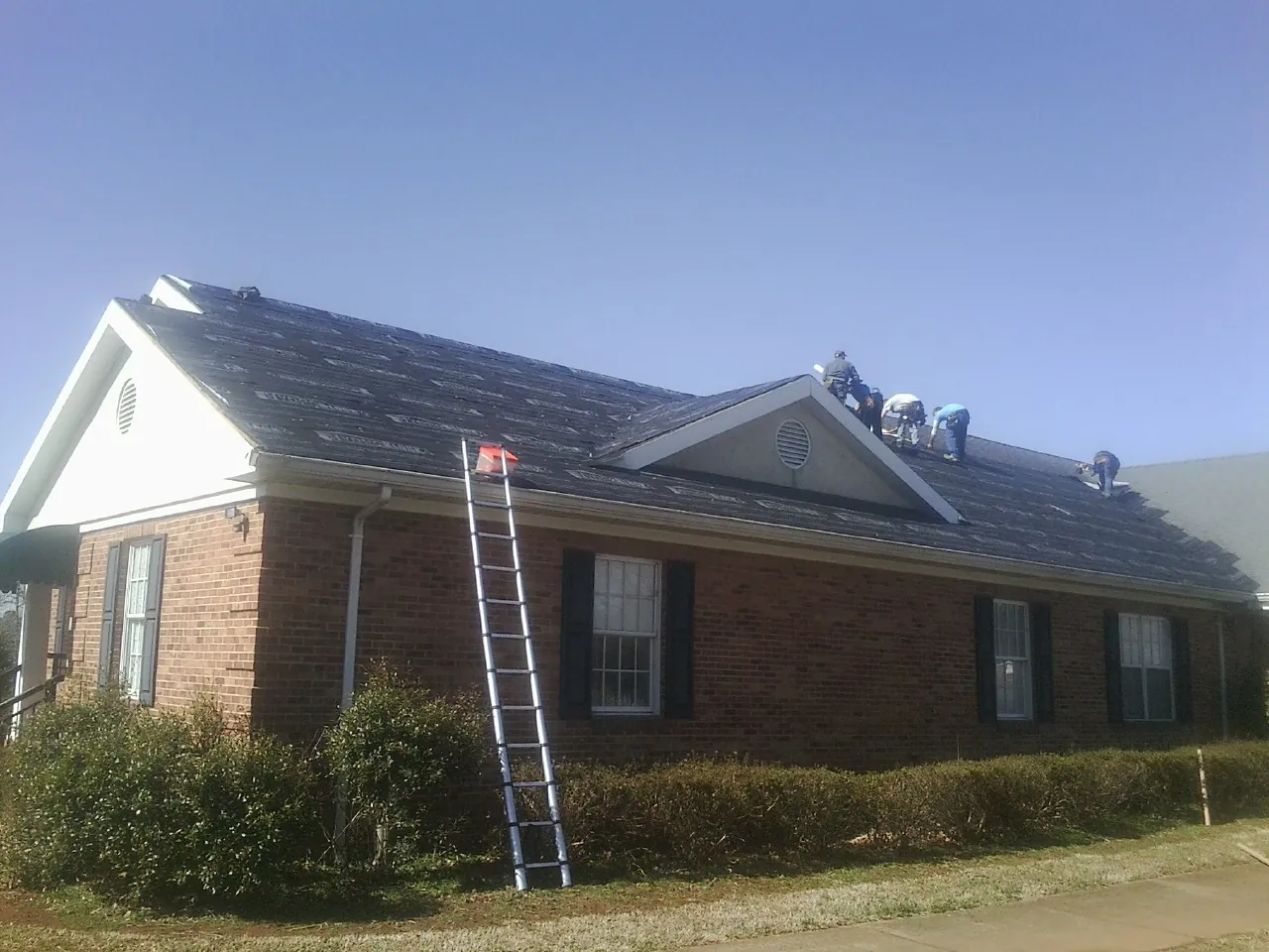 Crew tearing shingles off a brick ranch roof with a ladder set — Emergency Roof Repair work by our crew in House Springs