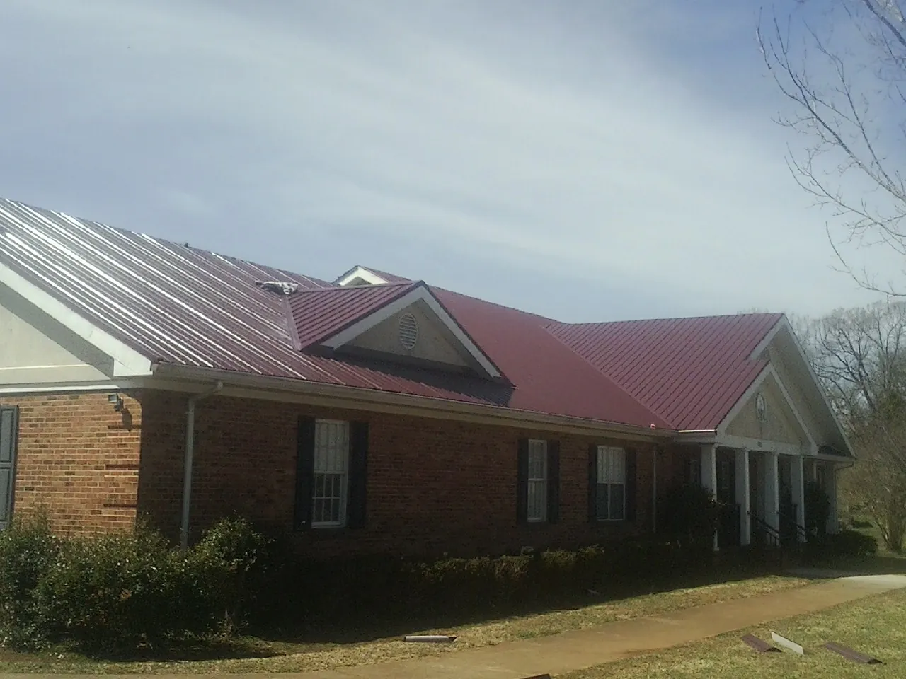 Red metal roof with gabled entries on a long brick building, from a Hail Damage Roof Repair job in House Springs