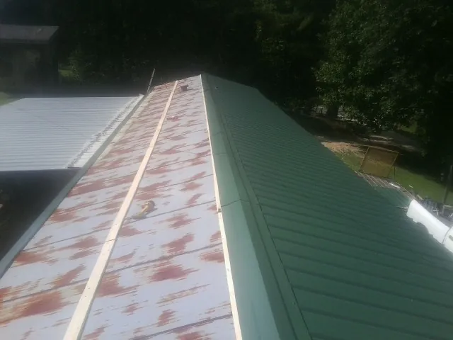 Old rusted panels beside newly installed green metal roofing — Wind Damage Roof Repair by Roofing Brothers in House Springs