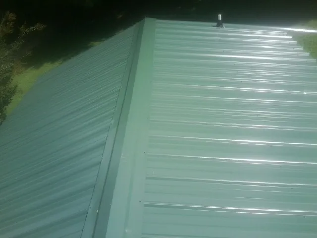 New green metal panels meeting at the ridge of a roof — Flat Roof Repair work by our crew in House Springs