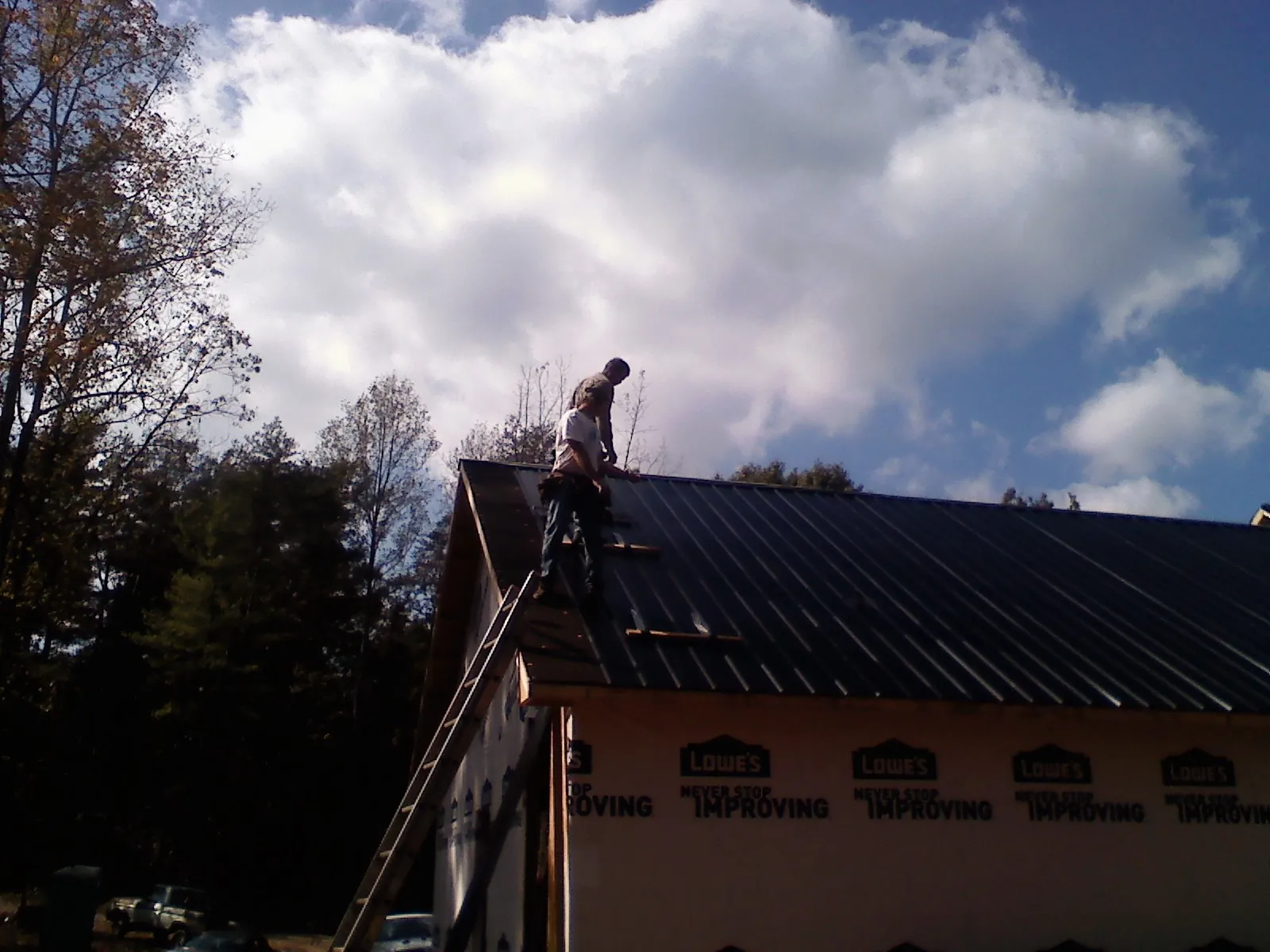 Roofer fastening dark metal panels high against a cloudy sky, from a Roof Inspection job in House Springs