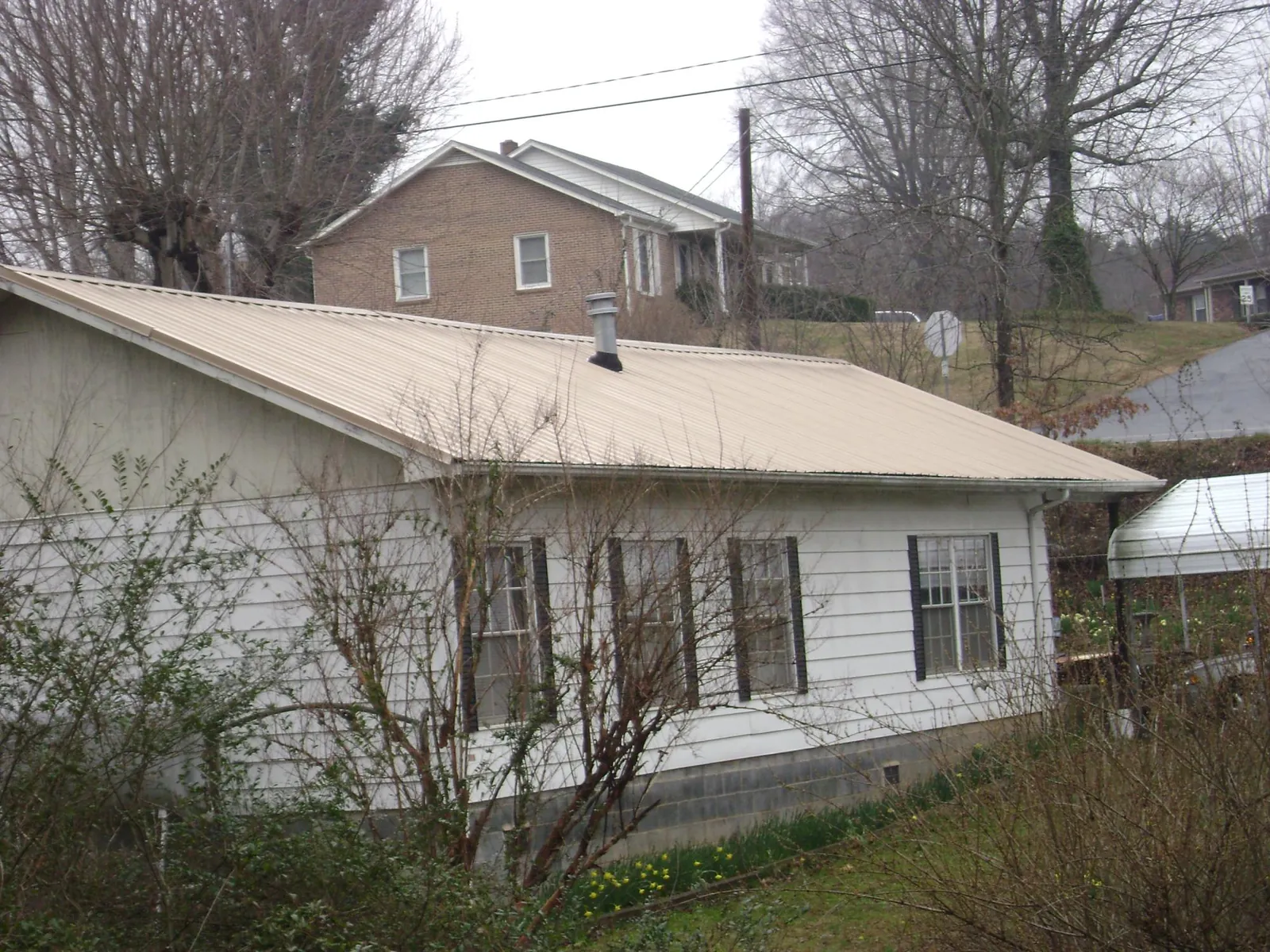Tan metal roof on a white sided house set into a hillside — Commercial Roofing by Roofing Brothers in House Springs